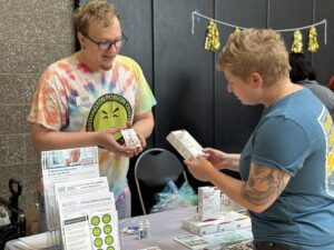 Young man in a Washington Poison Center shirt demonstrating naloxone to a woman