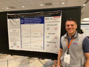 Man is his 30s standing in front of an educational poster