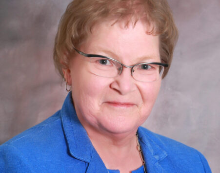 Older woman with short light brown hair and glasses in a blue suit.