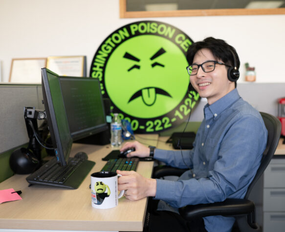 Man in headset typing on computer wile looking up and smiling with a Washington Poison Center Mr. Yuk logo sign in the background