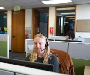 Blond woman with a headset looking at computer and talking