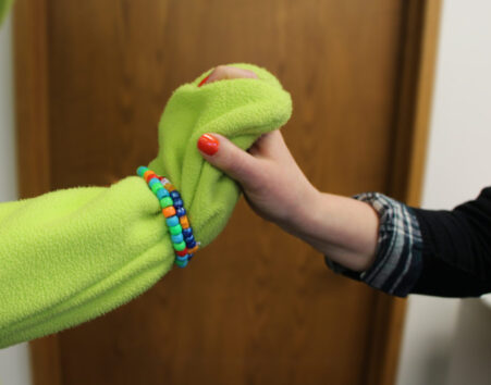 Green Mr. Yuk mascot and human hands holding.