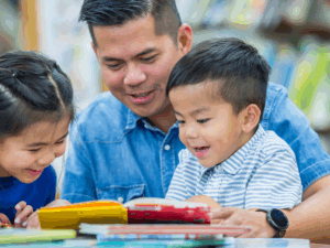 Dad with two young kids looking down at a book and smiling